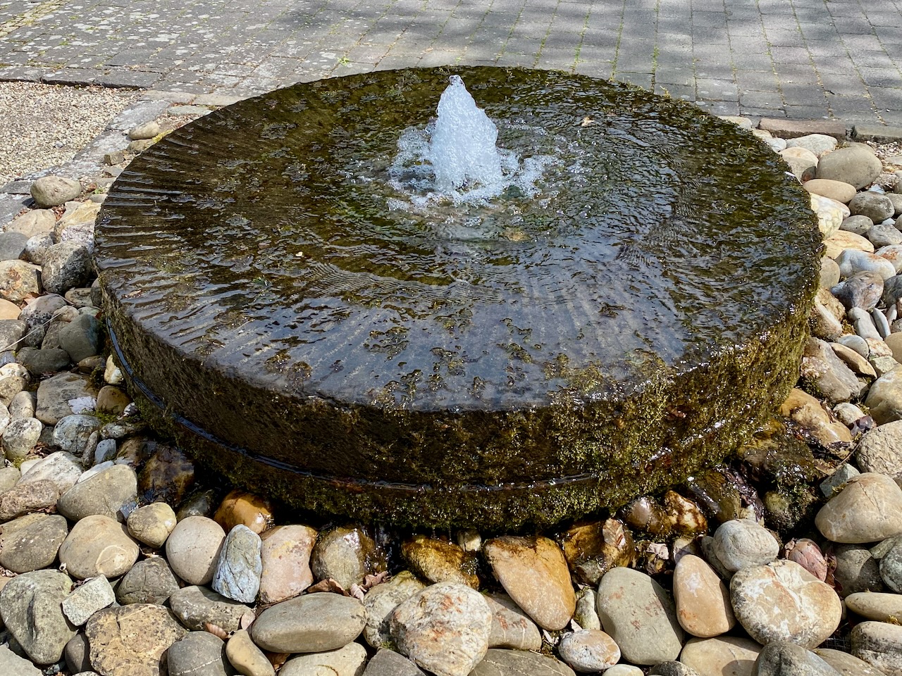 Brunnen auf Steinscheibe umrandet von großen Kieselsteinen
